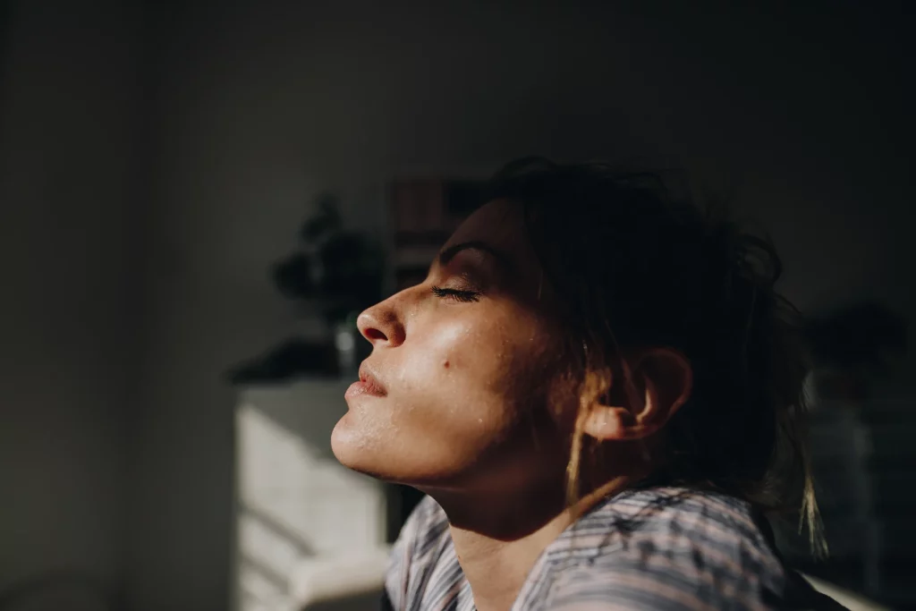 A woman with closed eyes, enjoying the warmth of the sun on her face at home. Counselling with Kim offers relaxation and emotional well-being support through online and in-person sessions.