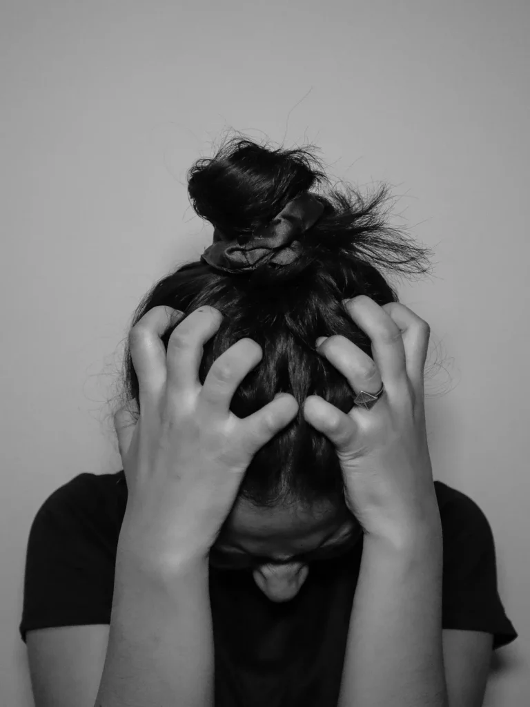 A stressed woman holding her head, looking down. Counselling with Kim offers counselling and cognitive hypnotherapy to manage stress and anxiety.